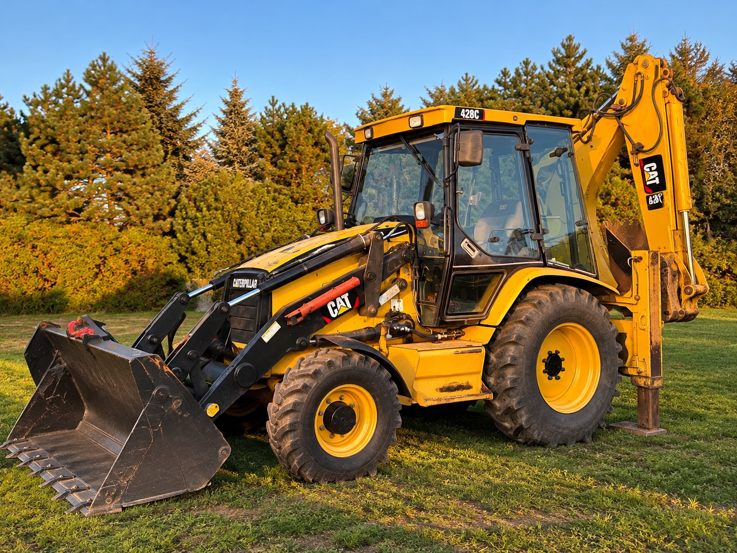 Żółta koparko-ładowarka CAT 428C na trawie, widok z przodu i boku