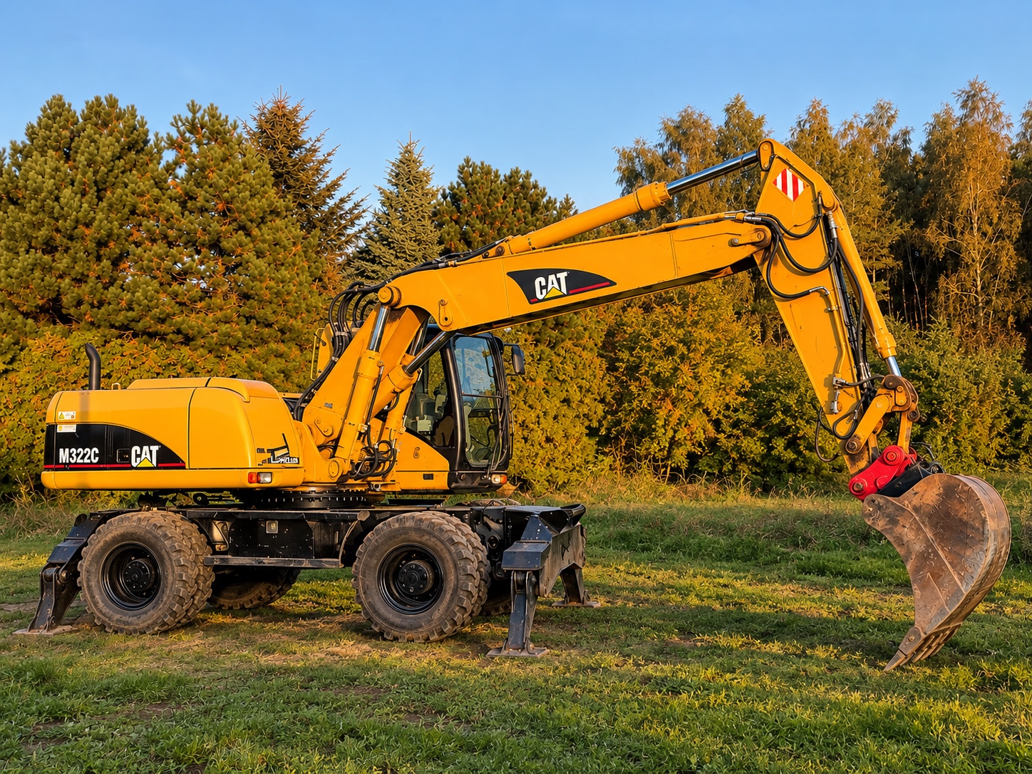 Żółta koparka kołowa CAT M322C na trawie, widok z boku